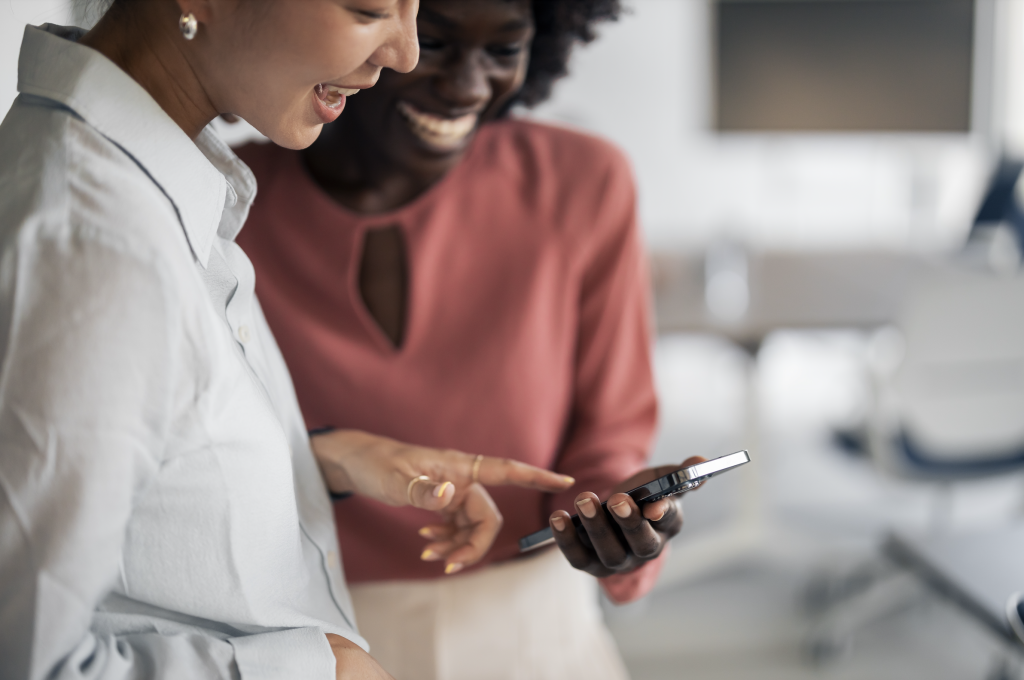 Two women looking at a phone, sharing a social media moment in person.